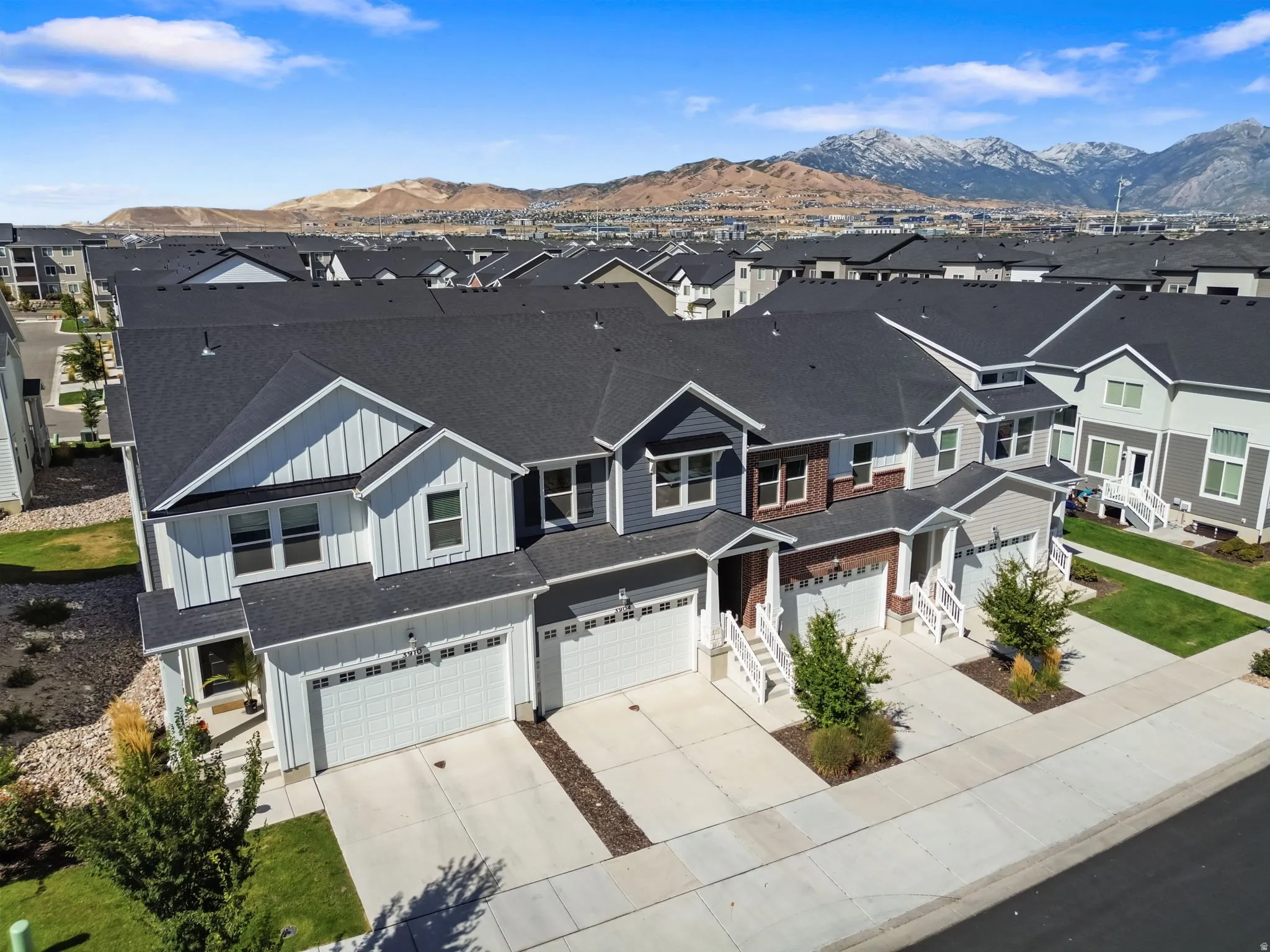 Contemporary townhome with board and batten siding, attached two-car garage, concrete driveway, and mature landscaping