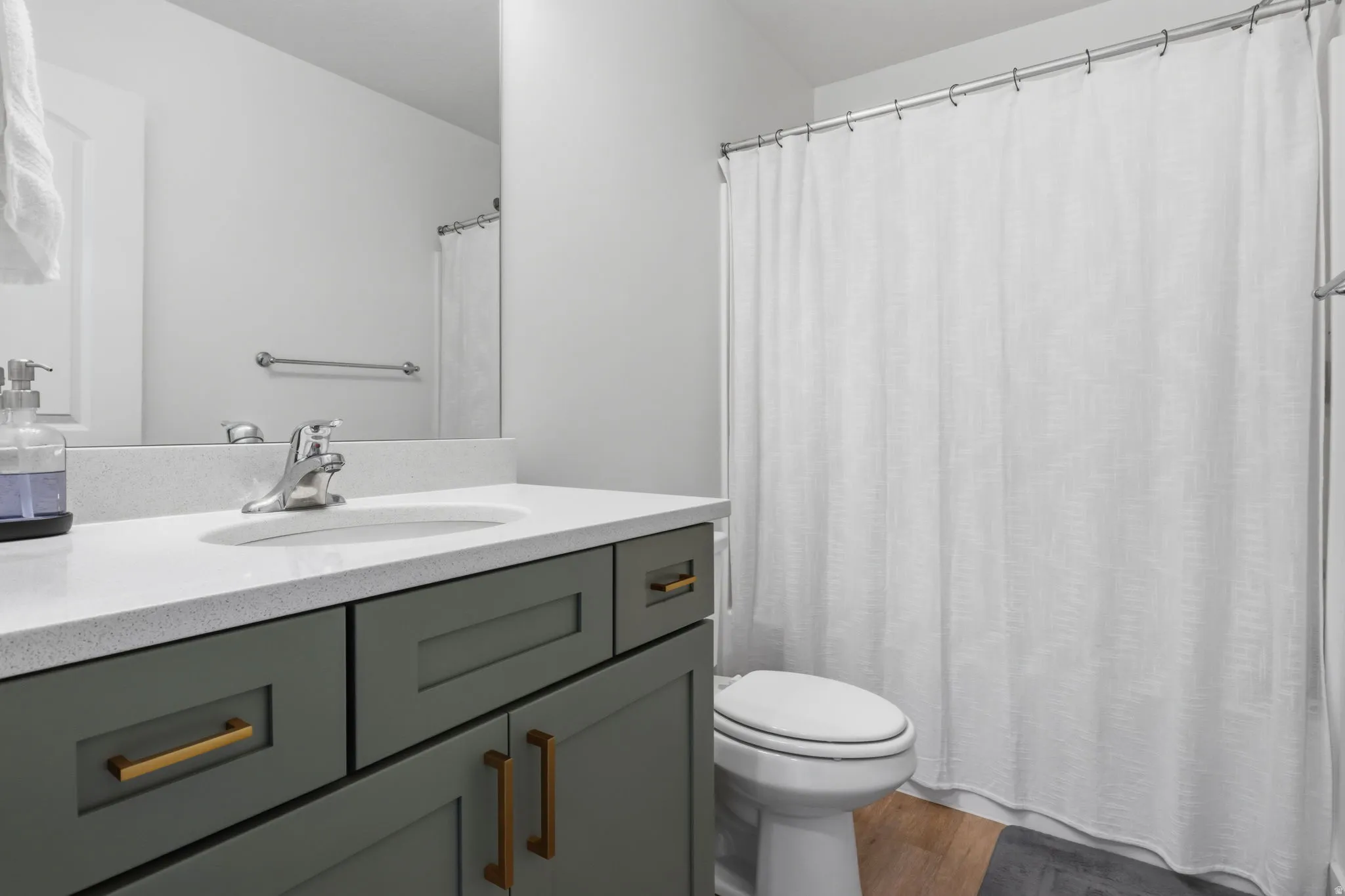 Vanity with a quartz countertop, integrated sink, and gray cabinetry with gold-finish hardware
