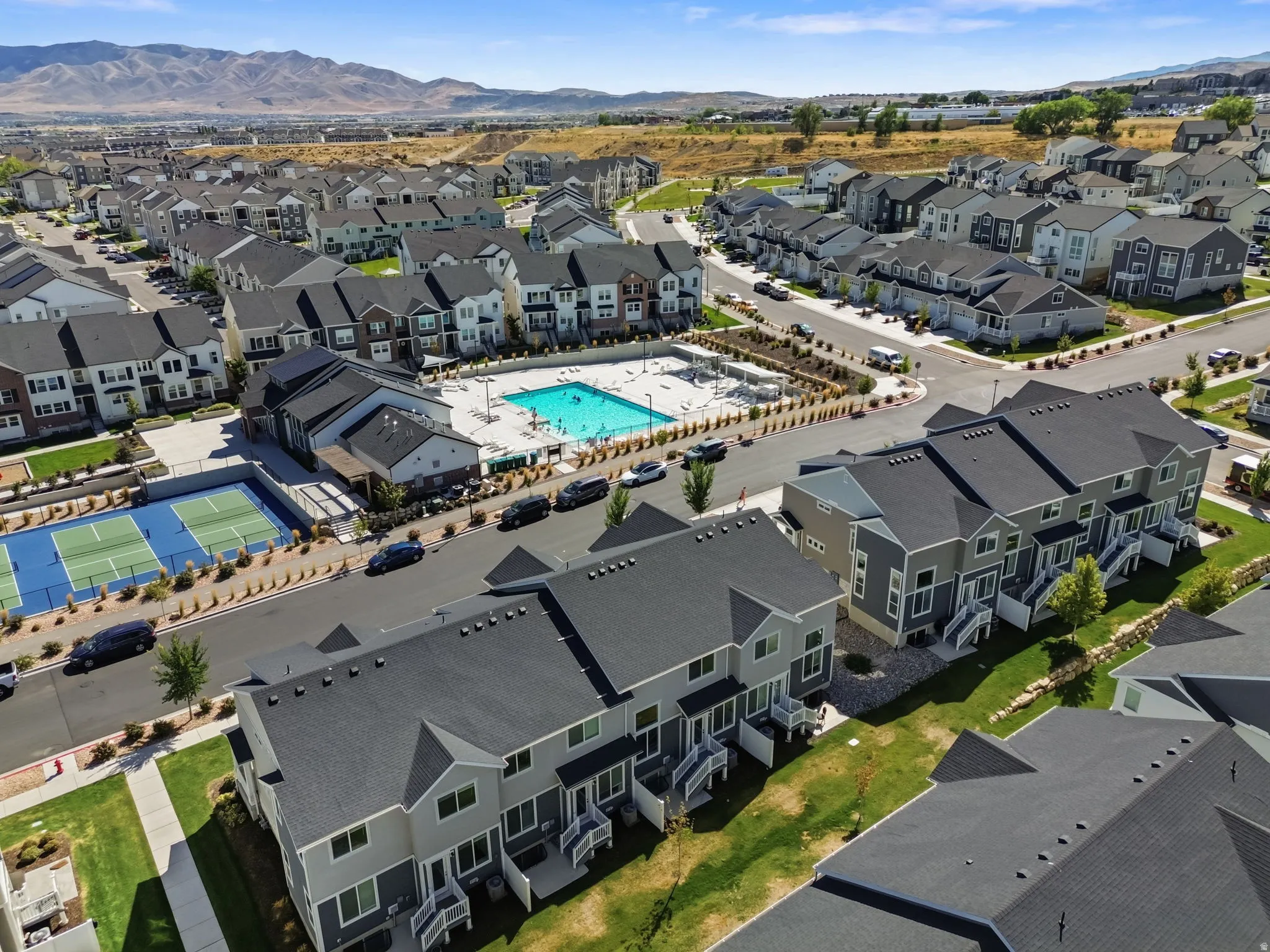 Community featuring a central swimming pool, multiple tennis courts, and contemporary townhomes with mountain backdrop