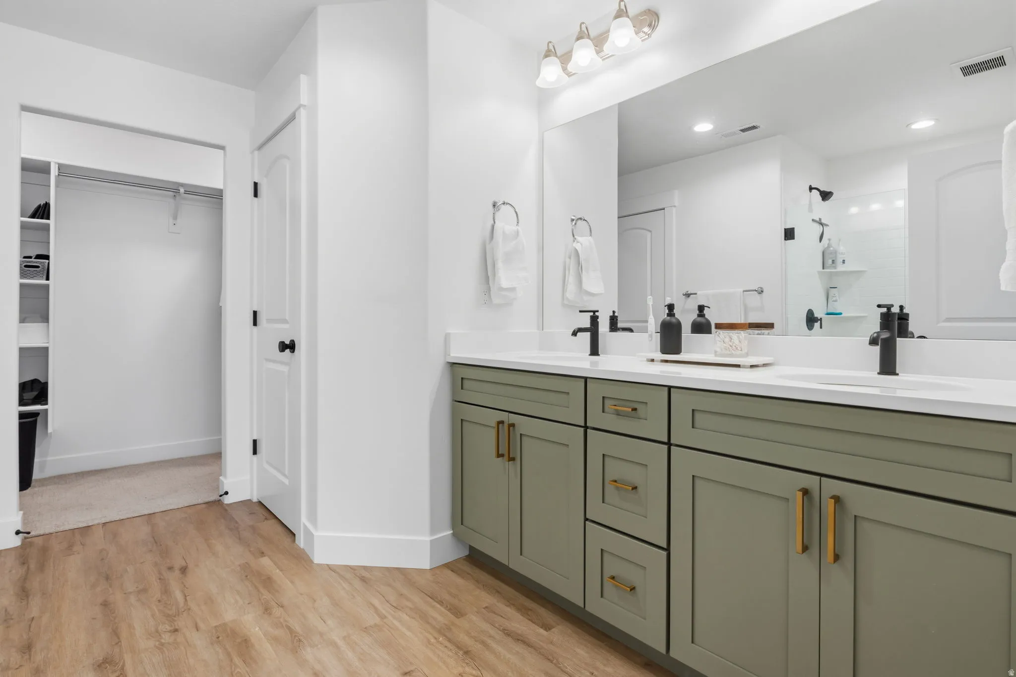 Dual vanity with white countertops, matte black faucets, and sage green cabinetry with gold hardware
