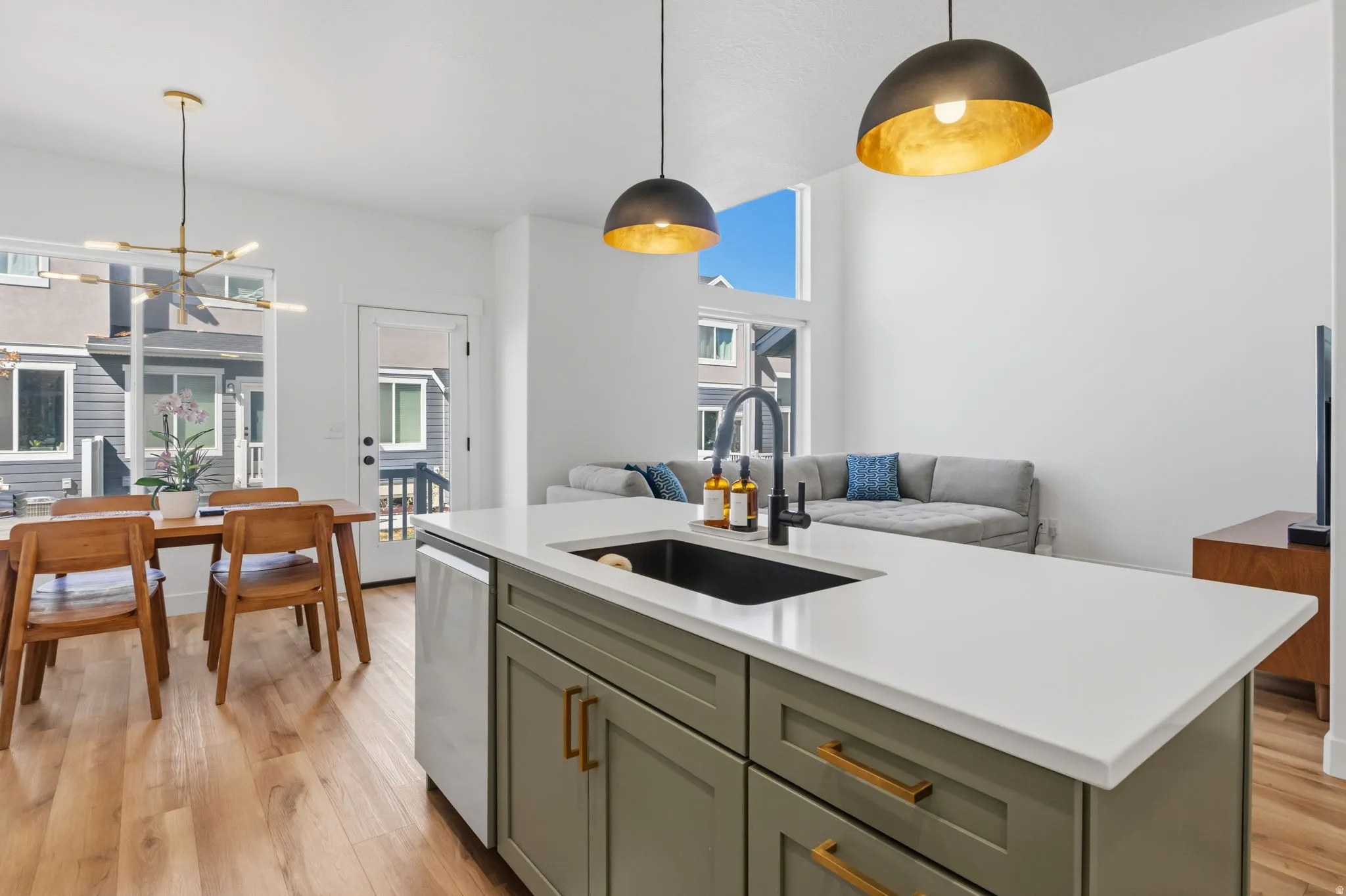 Kitchen island with an undermount sink and matte black faucet, light wood-finish flooring, a contemporary chandelier, and high ceilings