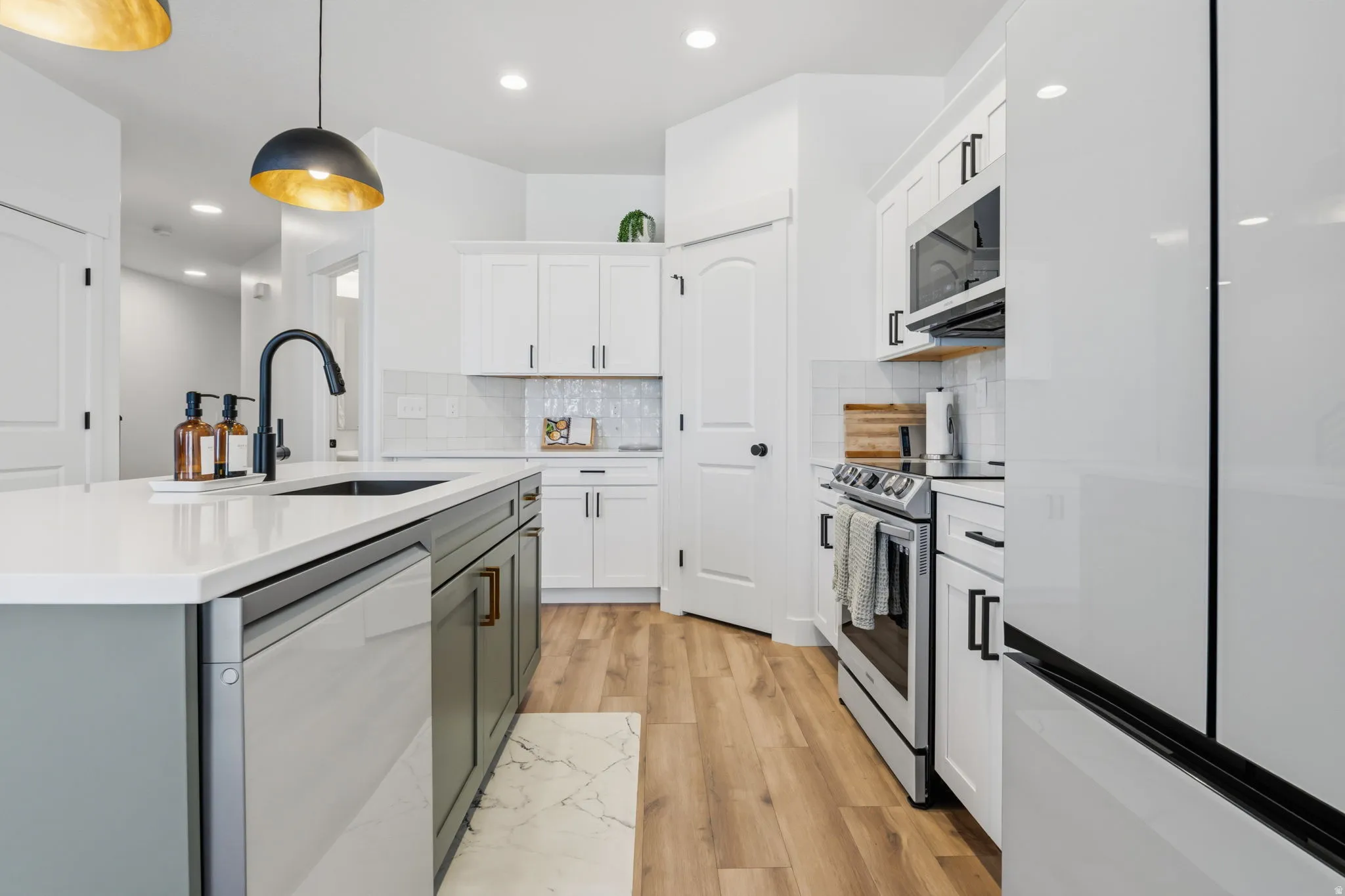 Kitchen featuring a large island with an integrated sink and matte black faucet, white shaker cabinetry, stainless steel appliances, and wood-finish flooring