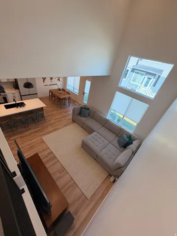 Open-concept living space with vaulted ceilings, large windows, wood-finish flooring, and a kitchen island with seating