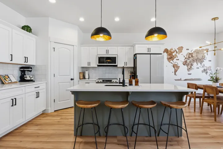 White cabinetry with matte black hardware, light-toned wood-finish flooring, island with light countertop, built-in microwave, and stainless steel refrigerator