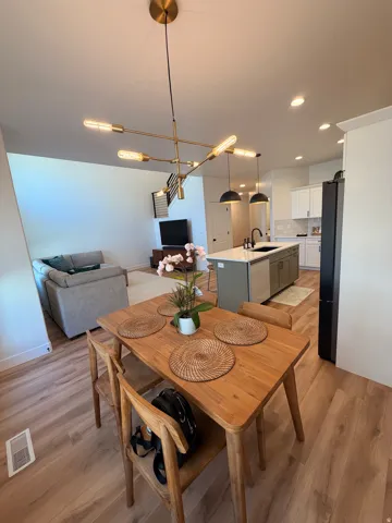 Open-concept living area with wood-finish flooring, a modern chandelier, recessed lighting, and a kitchen island with a dark sink and fixtures