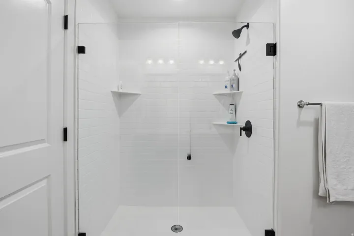 Glass-enclosed shower with white subway tile, a matte black shower head, and built-in shelving