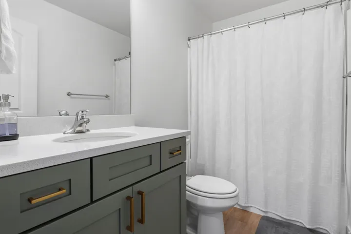 Vanity with a quartz countertop, integrated sink, and gray cabinetry with gold-finish hardware