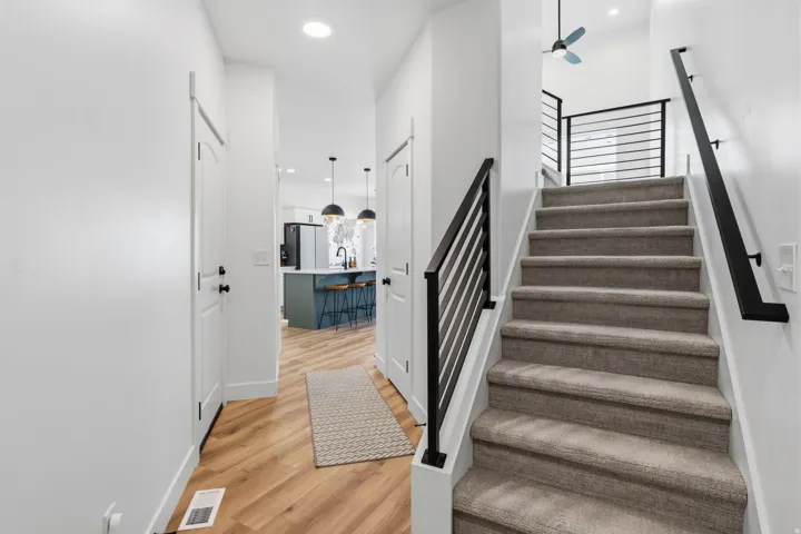 Wood-finish flooring, recessed lighting, white walls, and a staircase with carpeted treads and black metal railings