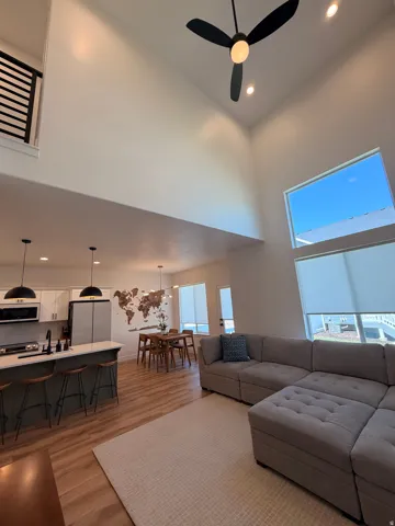Vaulted ceilings with recessed lighting, wood-finish flooring, kitchen island with seating, stainless steel appliances, and large windows with roller shades