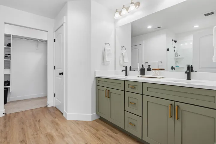 Dual vanity with white countertops, matte black faucets, and sage green cabinetry with gold hardware