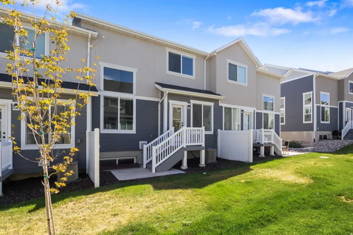 Multi-level exterior with a private patio area, white railings, and a manicured lawn