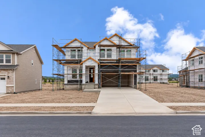 Two-story residence under construction featuring a concrete driveway, two-car garage, multi-gabled roofline, and front entryway