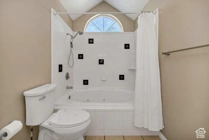 Vaulted ceiling with an arched window, white tiled tub surround with accent tiles, built-in jetted tub, and a chrome shower fixture.