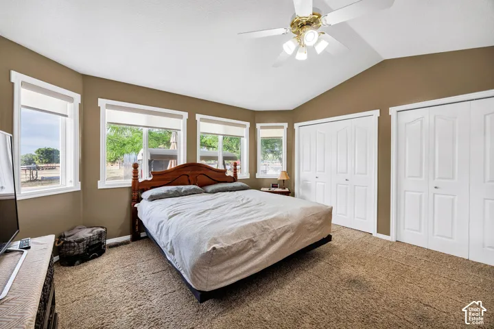 Vaulted ceiling, ceiling fan with lights, multiple windows, two double-door closets, and carpet flooring