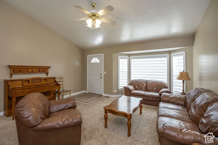 Vaulted ceiling with a ceiling fan, bay windows with blinds, front entry door with an arched window, and carpet flooring
