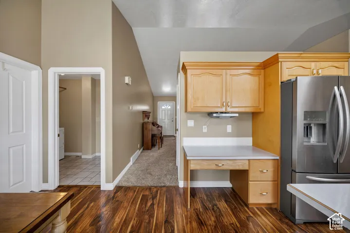 Wood-finish flooring with light wood cabinetry, stainless steel refrigerator, and built-in desk area