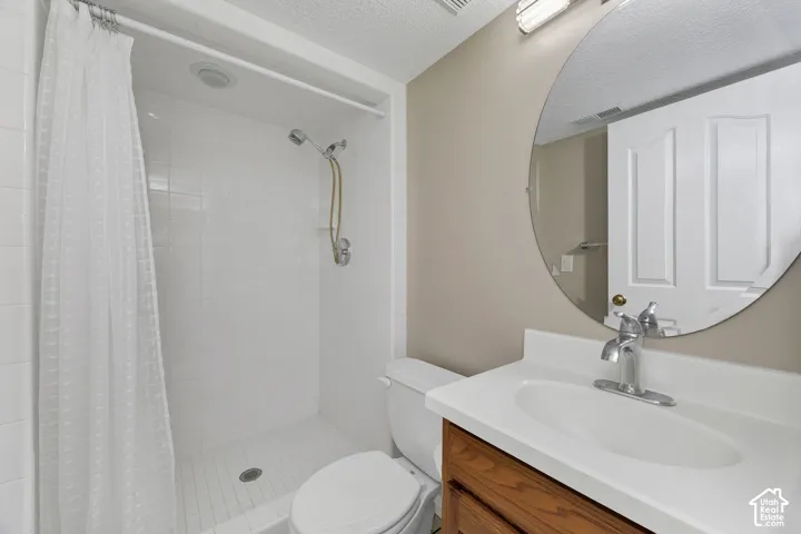 White tiled shower with a handheld shower fixture, wood-finish vanity with an integrated sink, polished chrome faucet, and a large circular mirror.