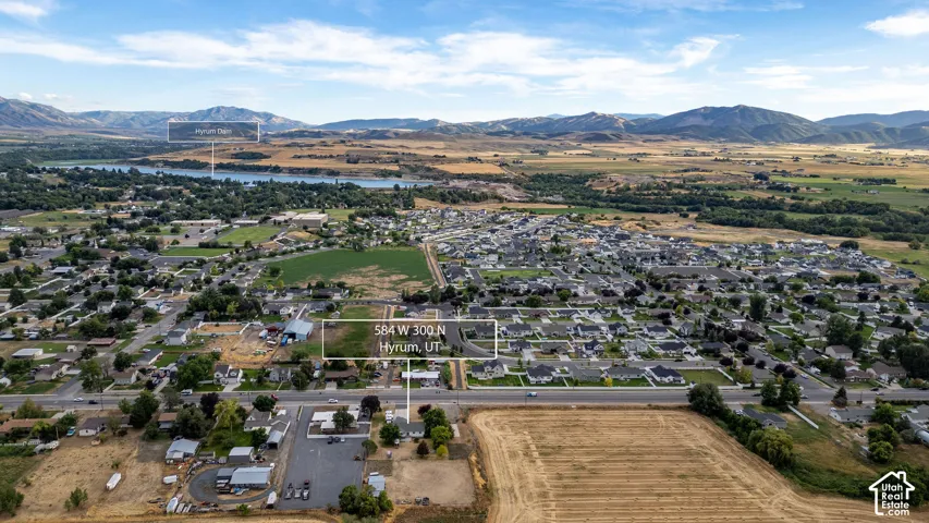 Aerial landscape featuring a developed residential area, expansive agricultural fields, a lake, and distant mountains.