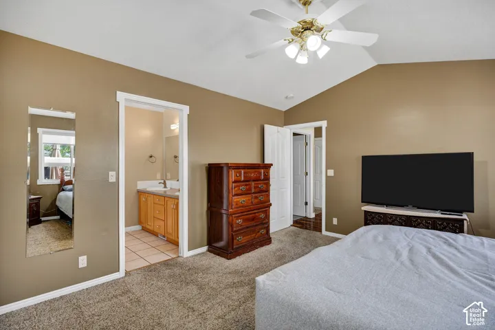 Vaulted ceiling with a ceiling fan, carpeted flooring, and en-suite bathroom with tile flooring and a wood-finish vanity