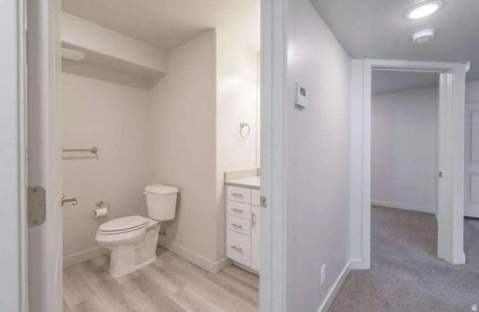 Powder room featuring a single vanity with stone countertop, white cabinetry, wood-finish flooring, and recessed lighting