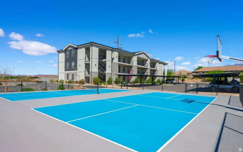 Multiple outdoor courts with blue surfacing, basketball hoop, and covered parking structure