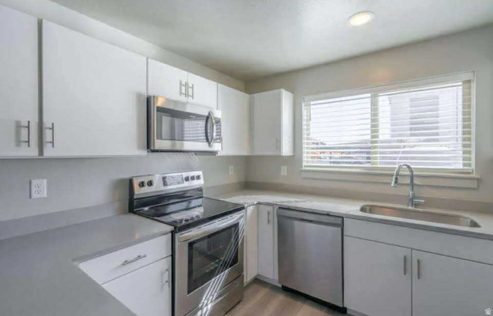 White cabinetry with contemporary hardware, stainless steel appliances, solid surface countertops, recessed lighting, and wood-finish flooring