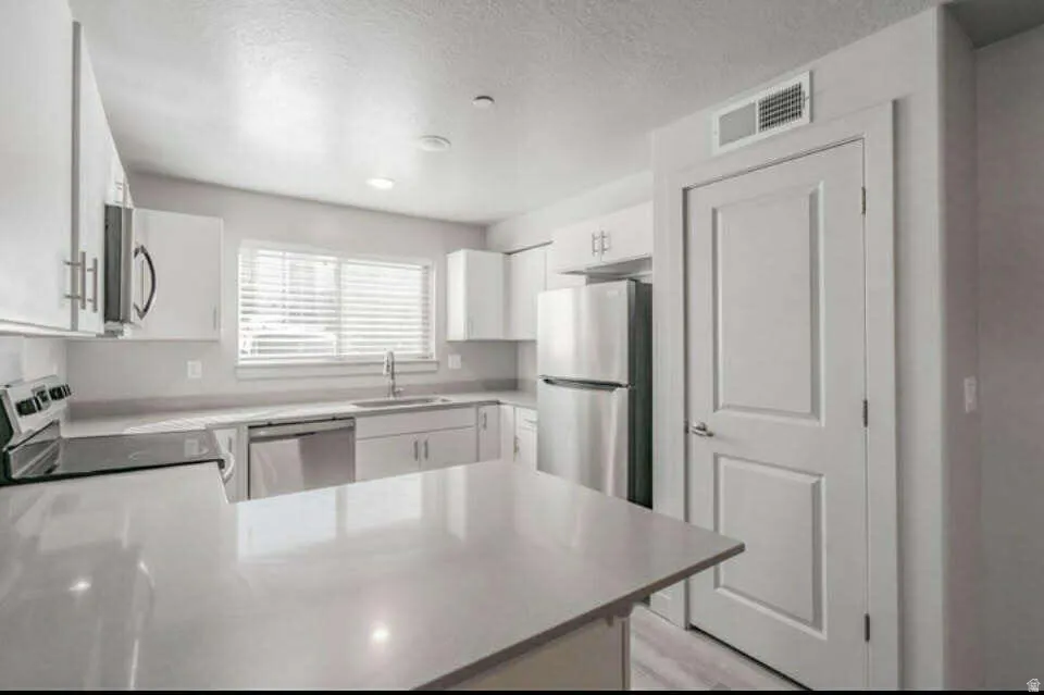Modern kitchen featuring white cabinetry, stainless steel appliances, a center island, and a window with blinds
