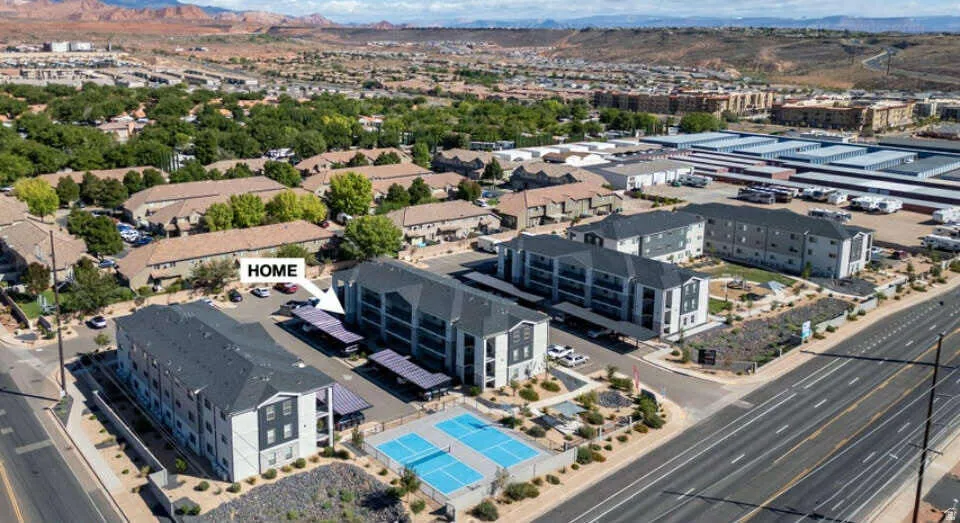 Modern multi-story building featuring covered parking, a tennis court, and an arid landscape design