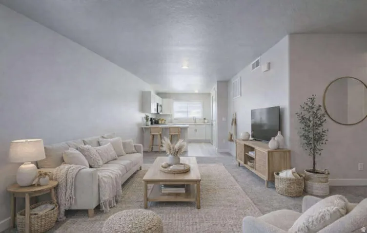 Open-concept living space featuring a carpeted area, hard-surface flooring, and a kitchen with white cabinetry