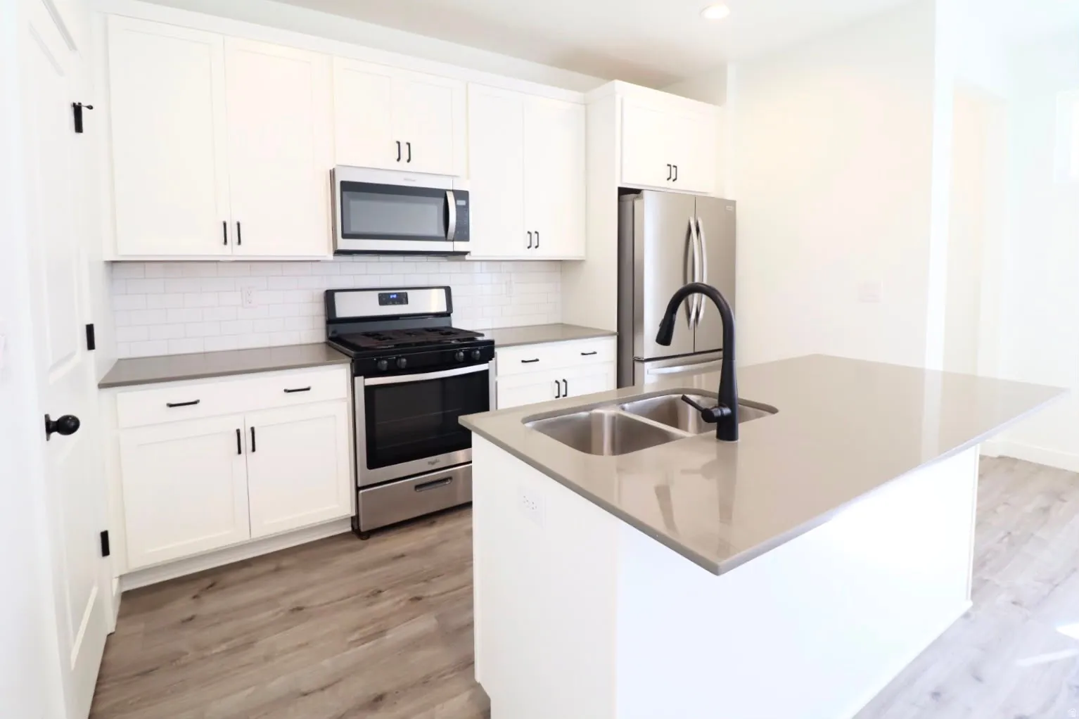 Modern kitchen featuring white shaker cabinetry, stainless steel appliances, a subway tile backsplash, and wood-finish flooring