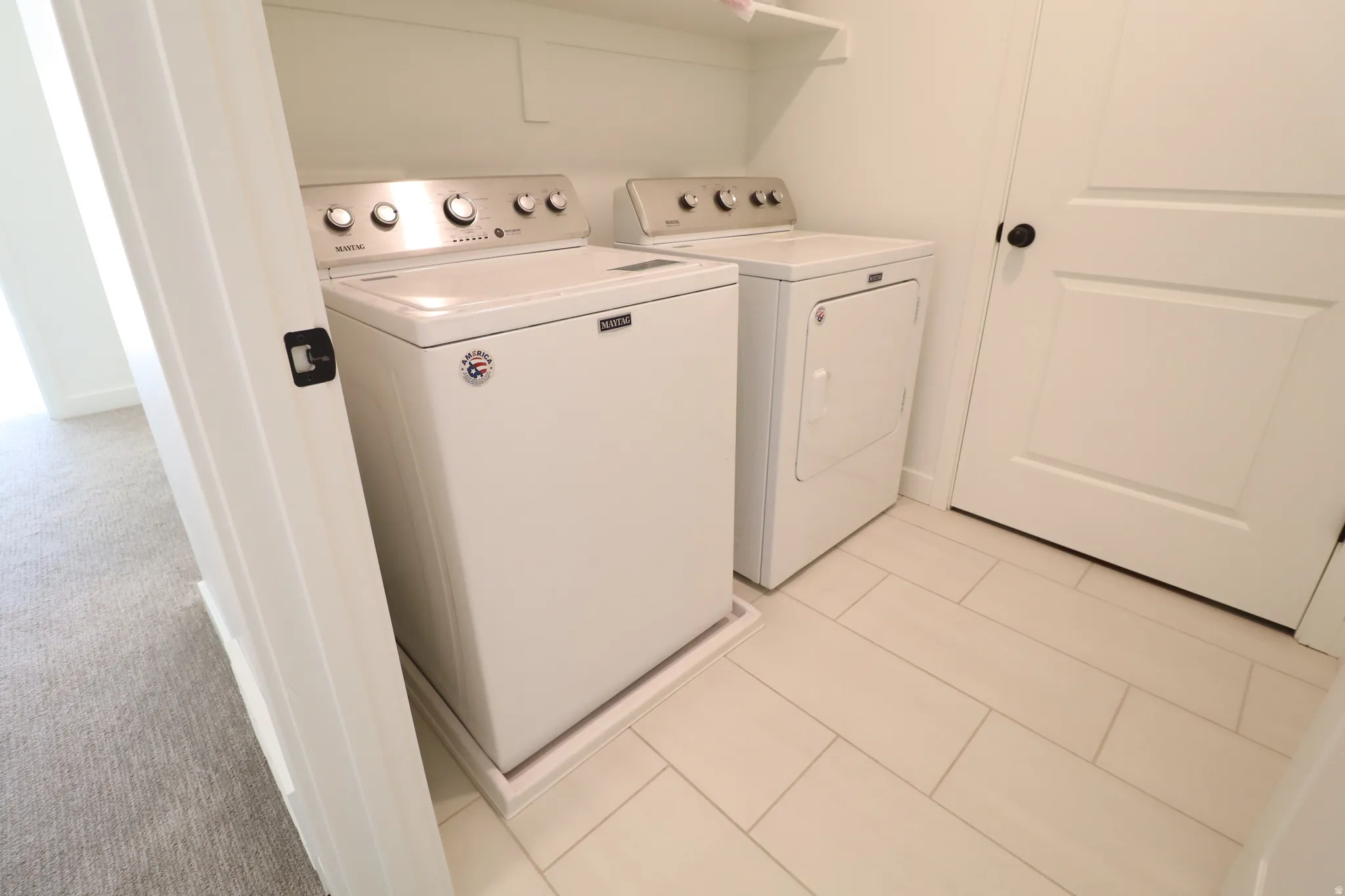 White tiled flooring, white walls, and a white interior door with a black handle