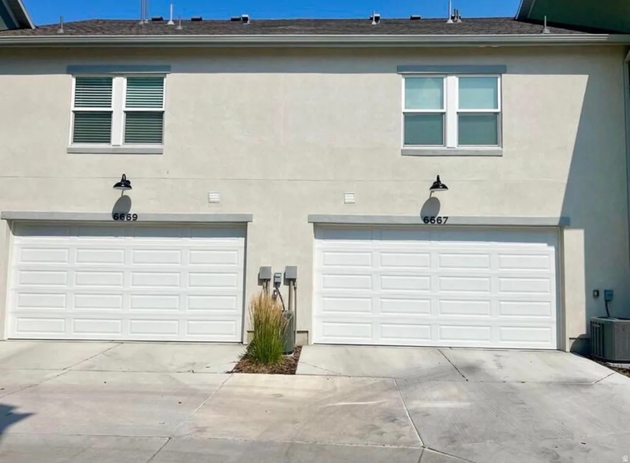 Stucco exterior with two white panel garage doors, each featuring an overhead black sconce light