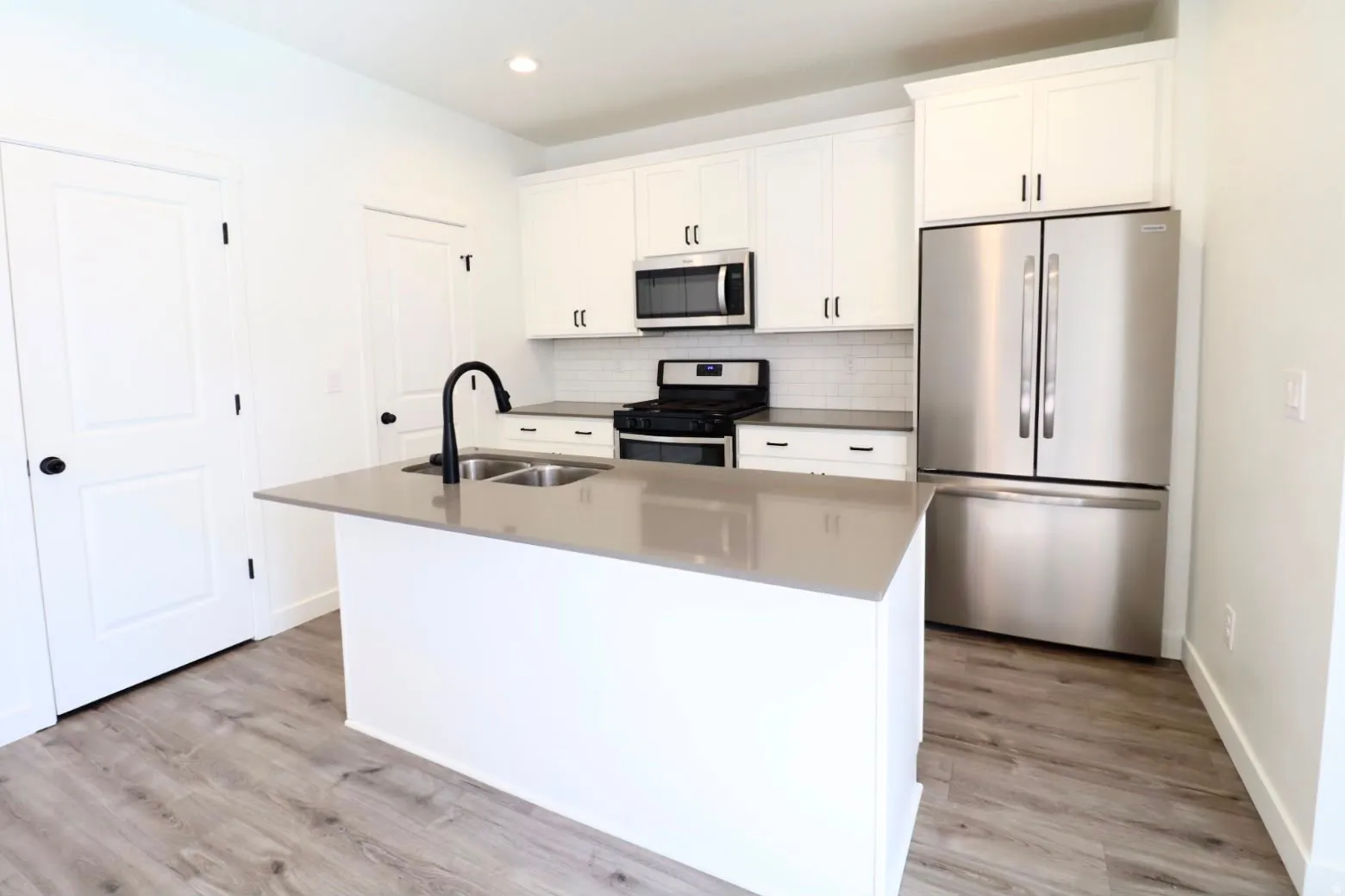 Kitchen featuring an island with double sinks, stainless steel appliances, white cabinetry, subway tile backsplash, and wood-finish flooring