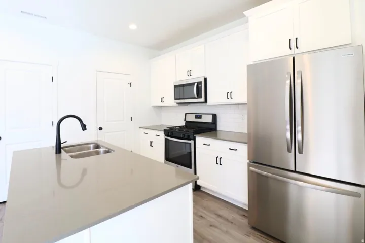Kitchen featuring stainless steel appliances, white cabinetry, a kitchen island with a double basin sink, light-colored countertops, and wood-finish flooring