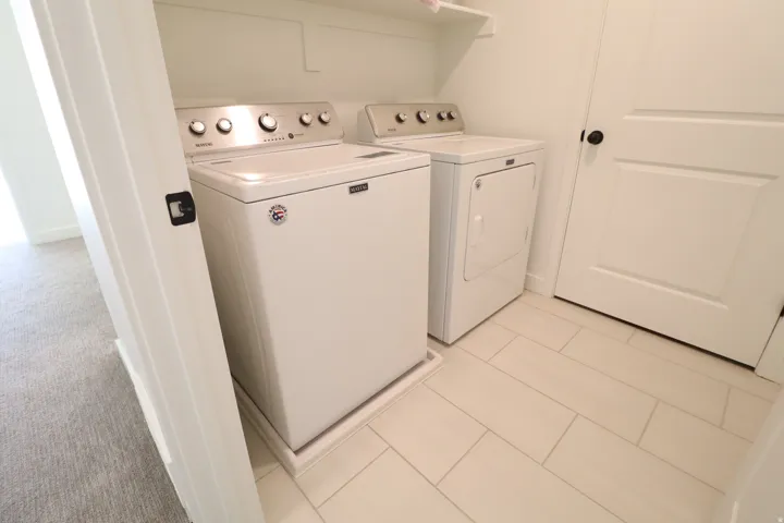 White tiled flooring, white walls, and a white interior door with a black handle