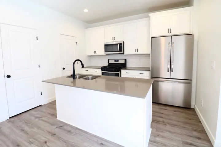 Kitchen featuring an island with double sinks, stainless steel appliances, white cabinetry, subway tile backsplash, and wood-finish flooring