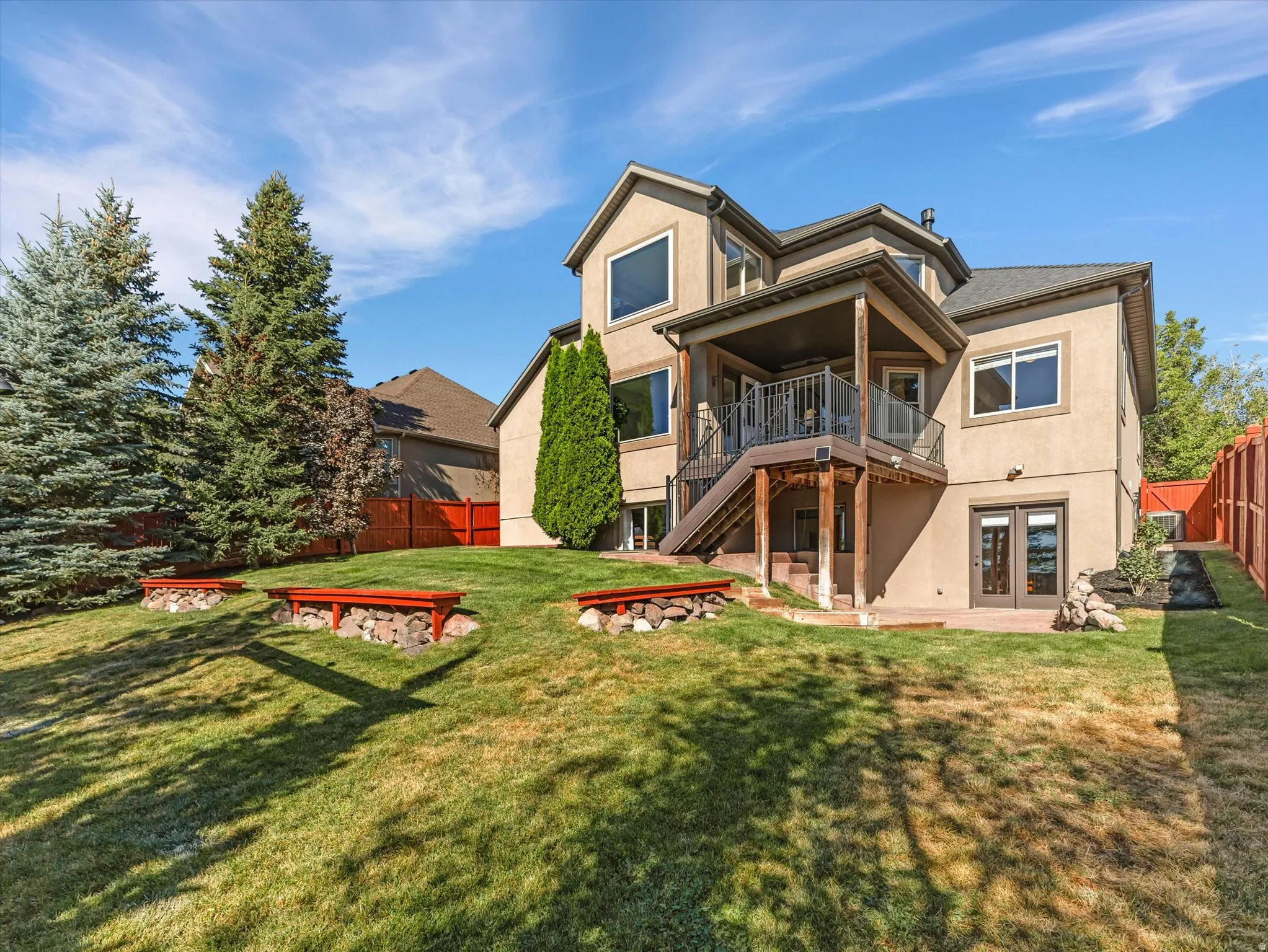 Exterior stucco finish, multi-level deck, ground-level patio, mature trees, and privacy fencing