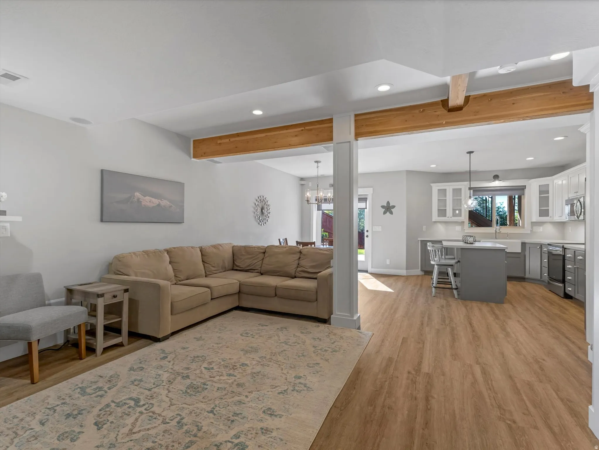 Open-concept living area featuring wood-finish flooring, exposed wood beams, a kitchen with an island, and a dining area with a chandelier