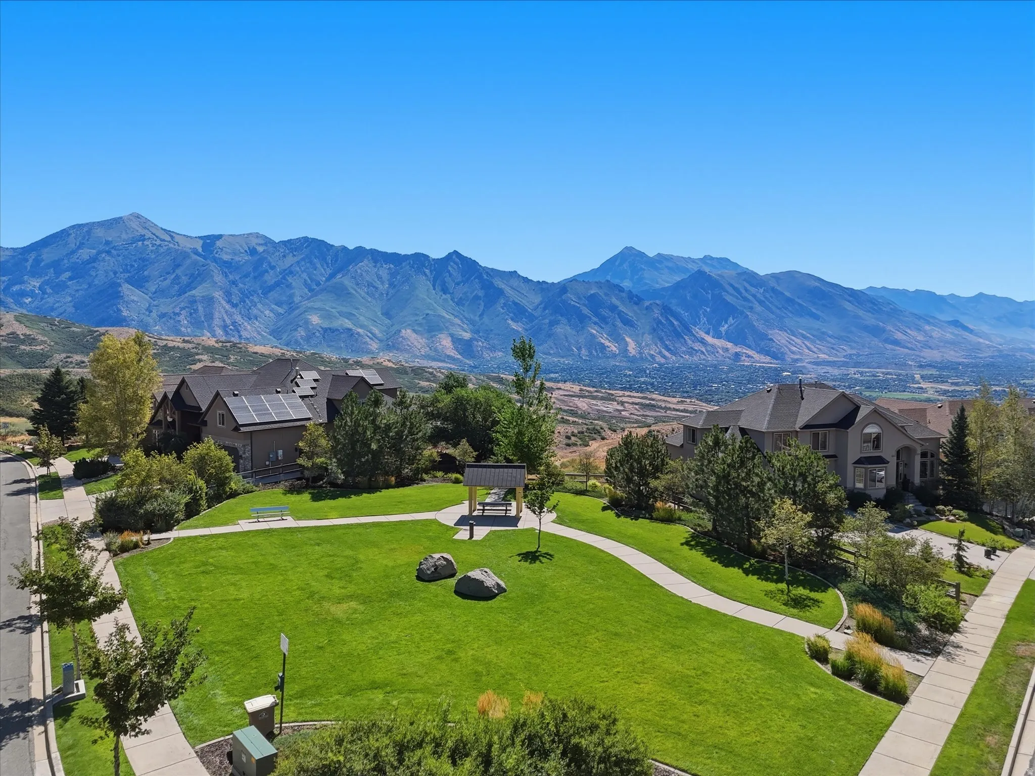 Expansive green space featuring a paved walkway, mature trees, and a mountain backdrop