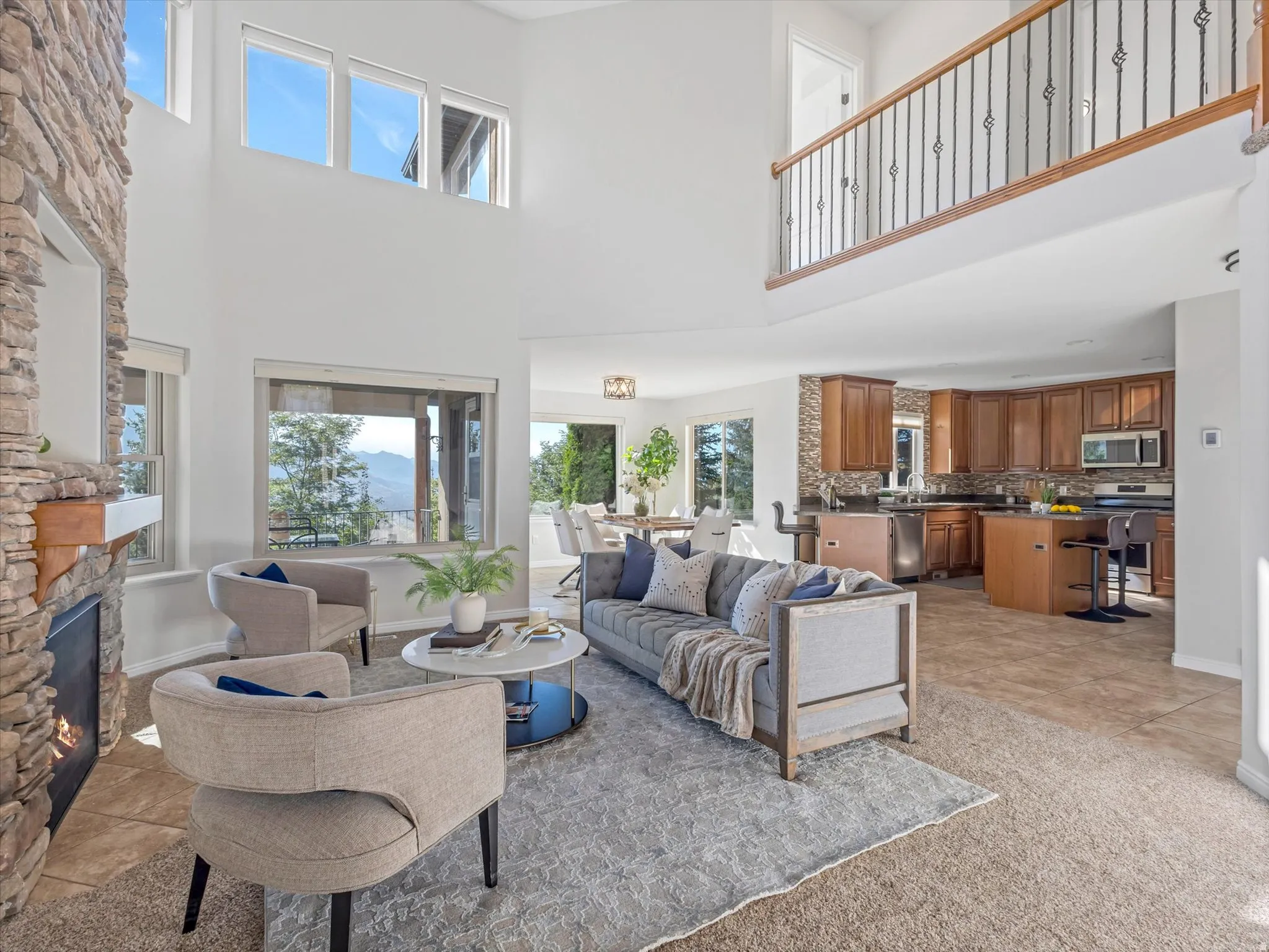 Two-story living area featuring a stone fireplace, high ceilings, and an open balcony