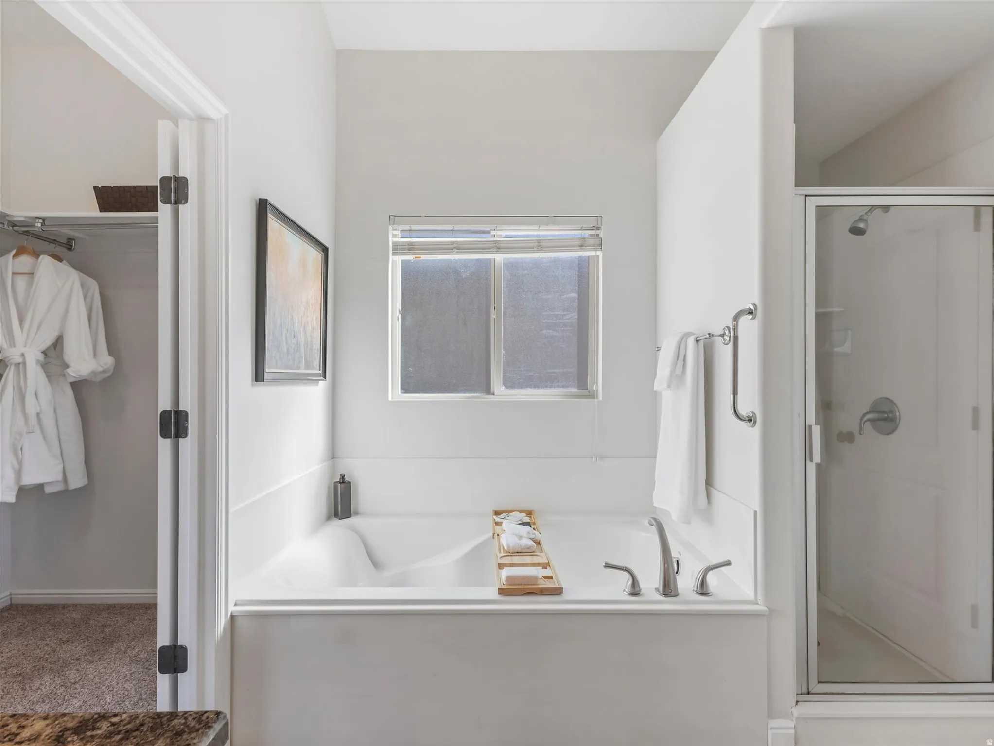 Built-in soaking tub with deck-mounted faucet, adjacent glass-enclosed shower, and a privacy window