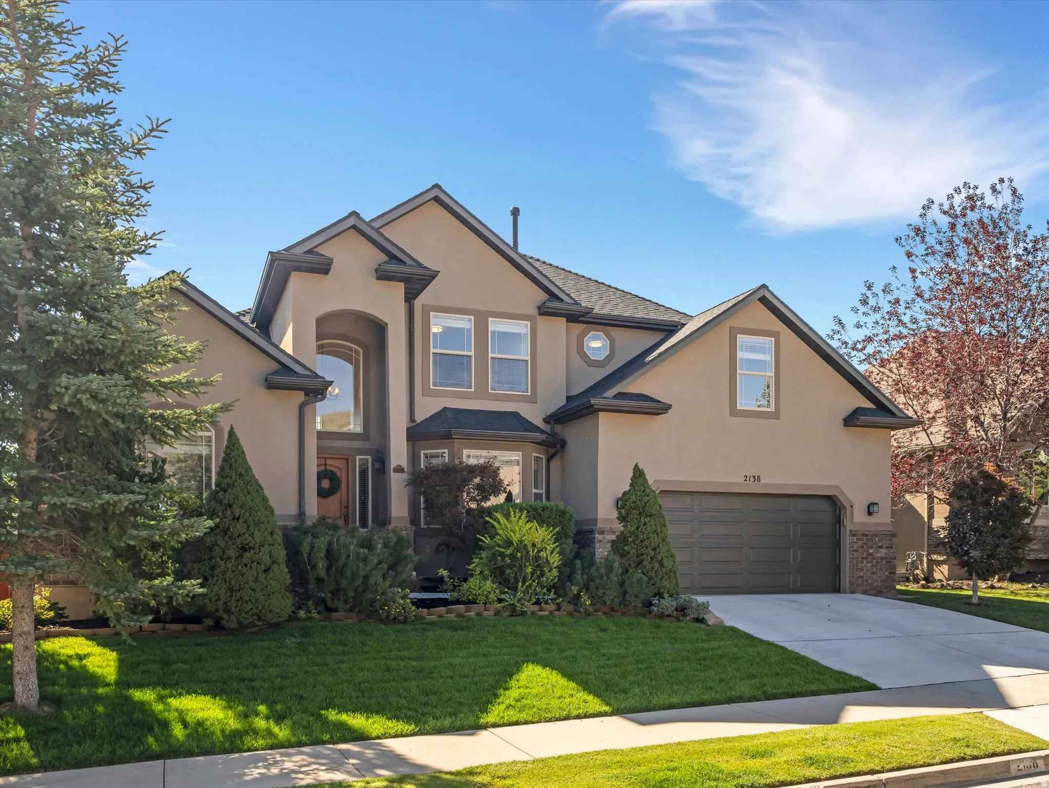 Stucco exterior with stone accents, arched entryway, bay window, attached two-car garage, and established landscaping
