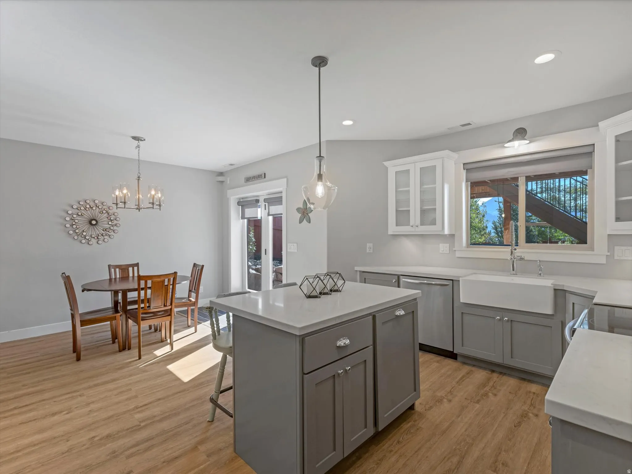 Kitchen featuring wood-finish flooring, two-tone cabinetry, farmhouse sink, stainless steel appliances, and a central island with a pendant light