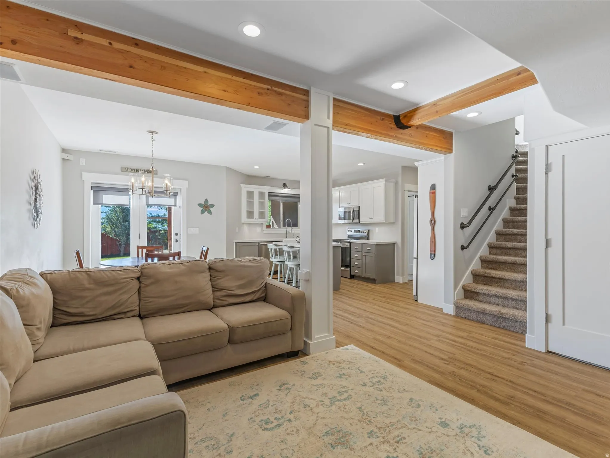 Exposed wood beams, wood-finish flooring, two-tone cabinetry, stainless steel appliances, and a carpeted staircase with black railings