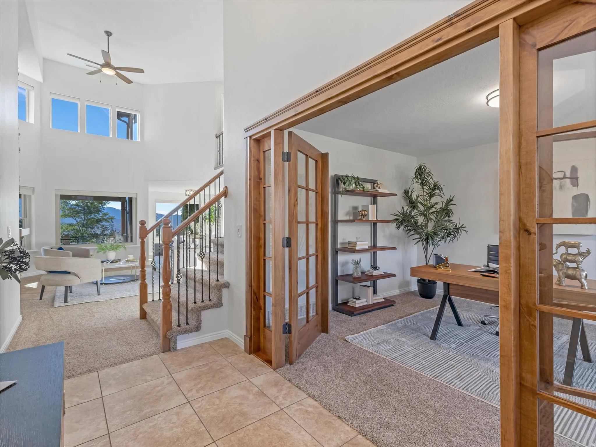 Two-story entry with a ceiling fan, a staircase featuring wood newel posts and wrought iron balusters, and a separate room with wood-frame French doors
