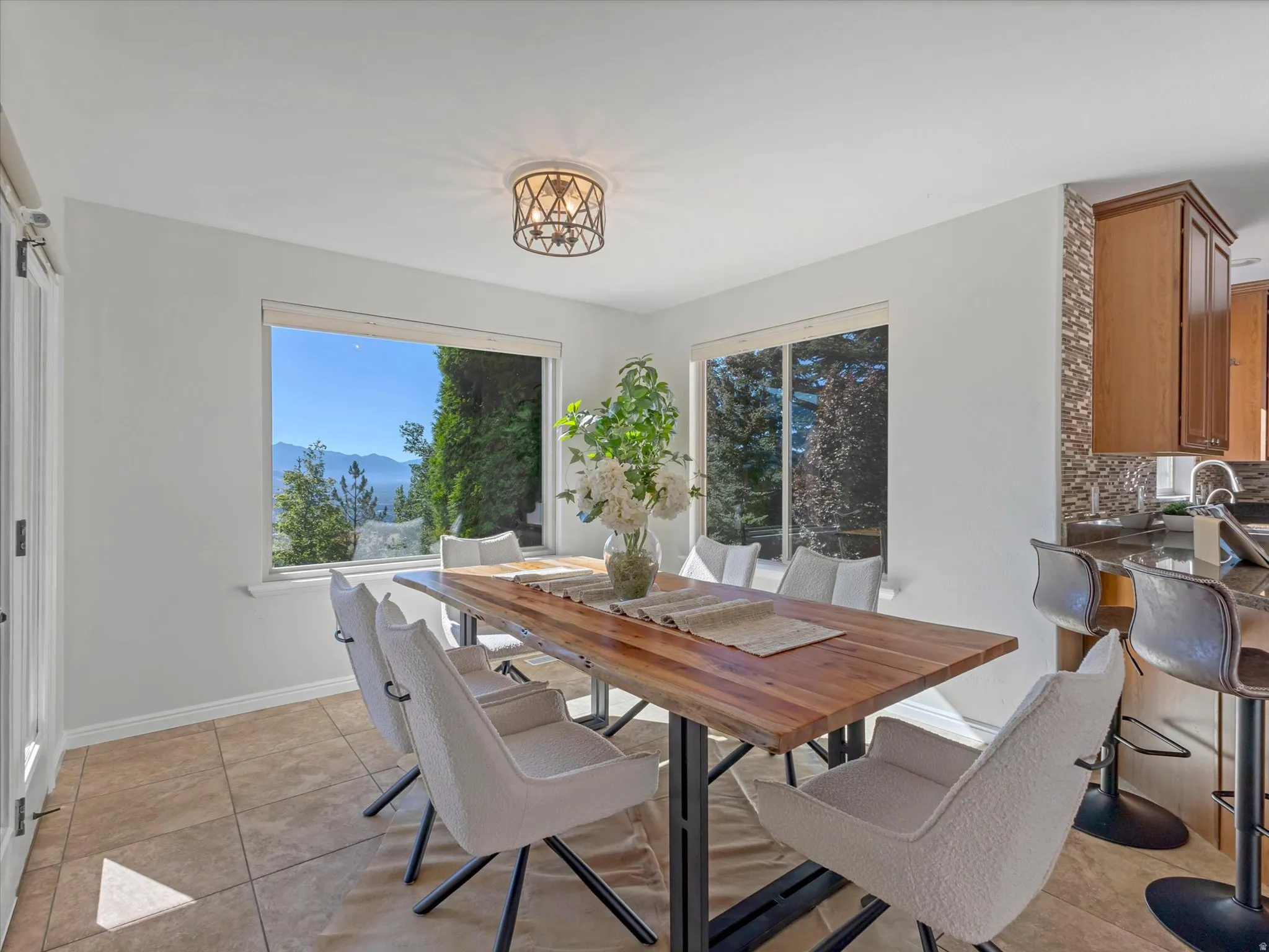 Tiled flooring, dual windows, mountain backdrop, decorative ceiling light fixture, kitchen pass-through