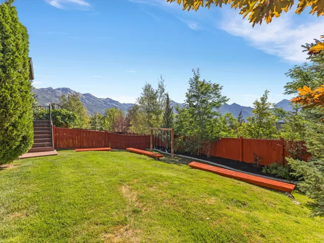 Expansive backyard with a manicured lawn, wood fencing, and mature trees