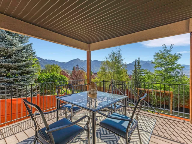 Covered outdoor deck with a slatted ceiling, dark wood-finish flooring, and black metal railings