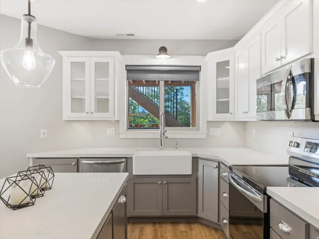 Two-tone cabinetry with glass-front upper cabinets, white apron-front sink, stainless steel microwave, and wood-finish flooring