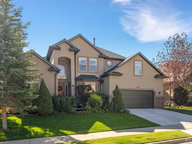 Stucco exterior with stone accents, arched entryway, bay window, attached two-car garage, and established landscaping